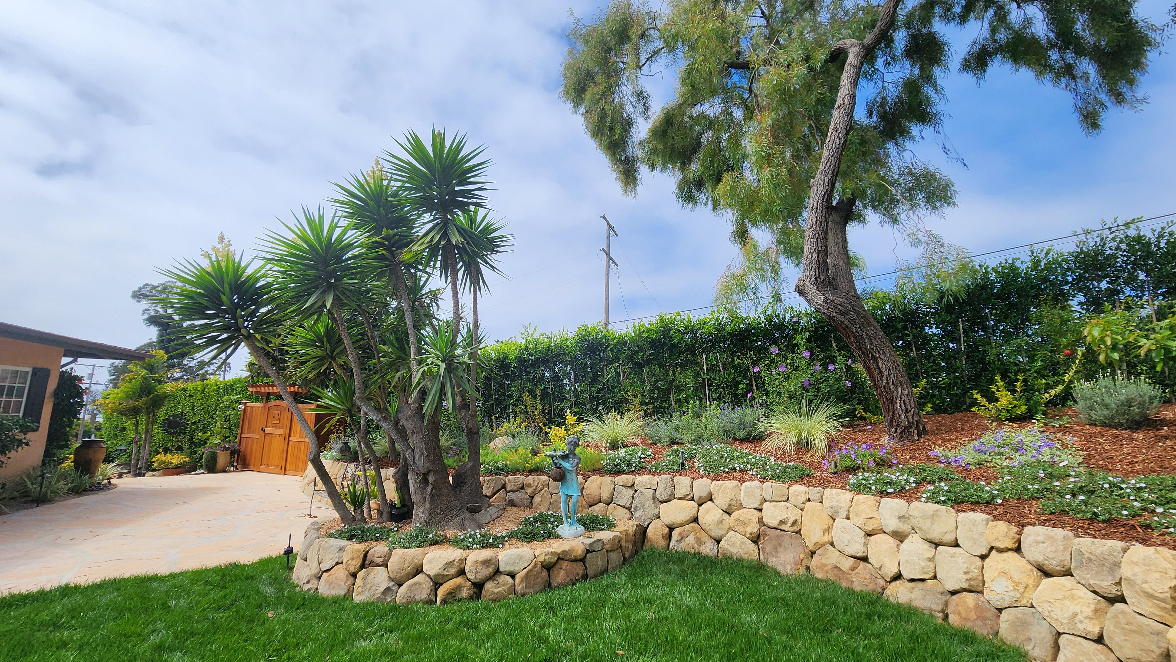 Curved natural stone retaining wall with tiered planting beds in a Santa Barbara garden, featuring a mature yucca tree.