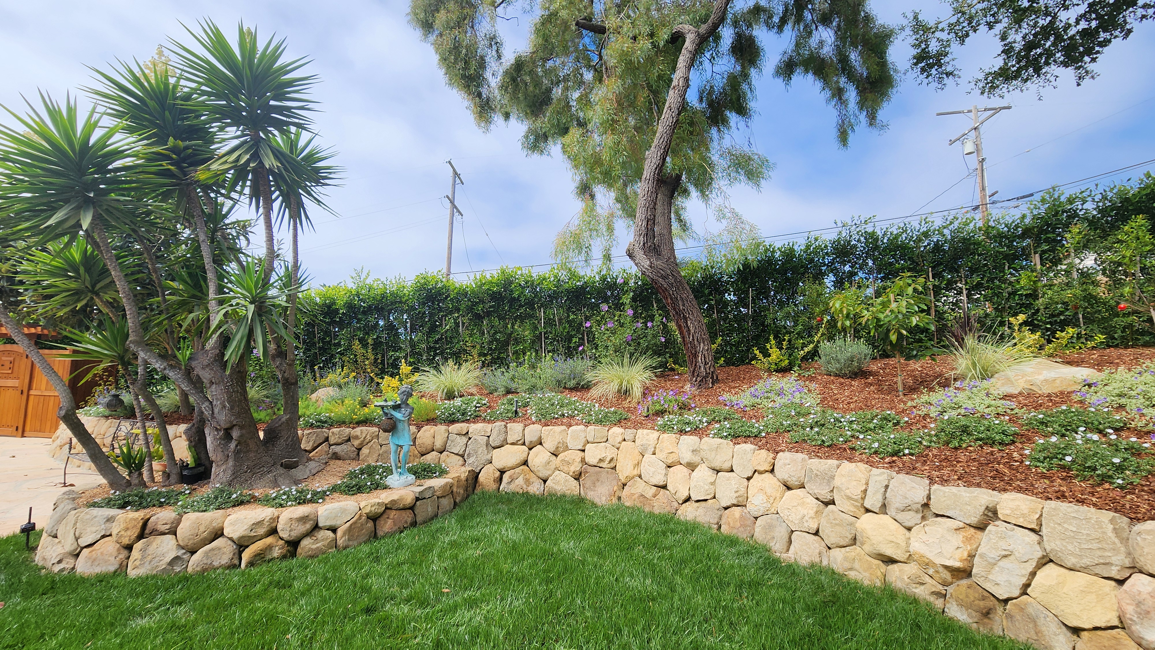Natural stone retaining wall creating a terraced garden bed in a Santa Barbara landscape with a garden statue accent.