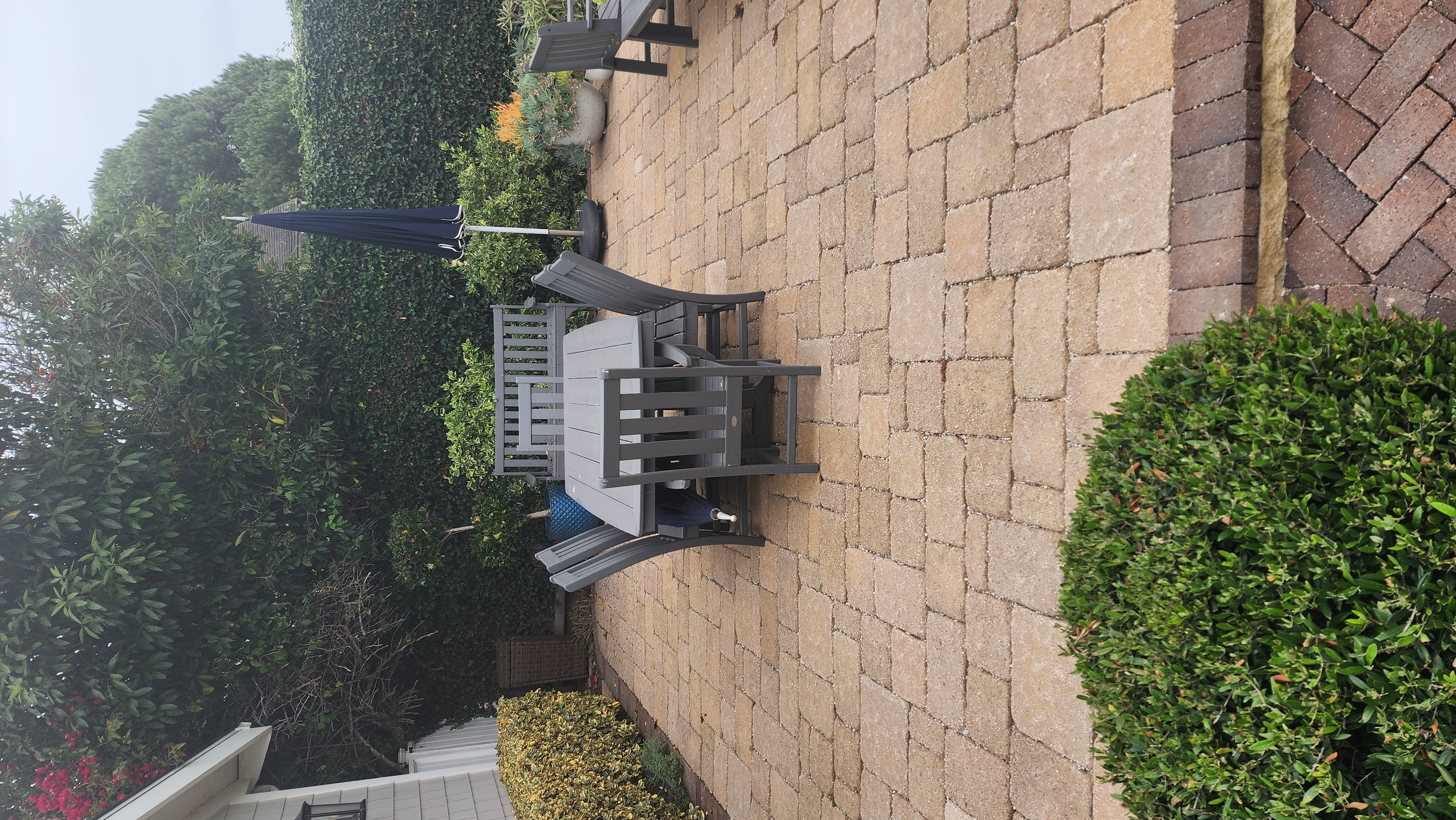 Outdoor dining patio with stone pavers and manicured hedges in a Santa Barbara garden.